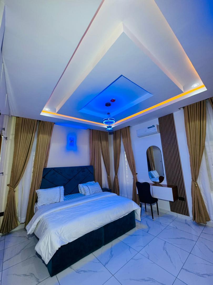 A bedroom lit in blue, with a navy headboard and a mirror